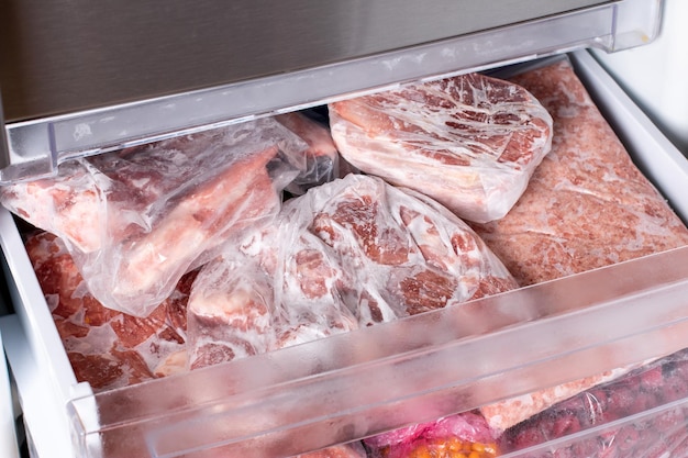 Meat in refrigerator freezer background. Closeup pork, meat and chicken leg in freezing compartment. Frozen food