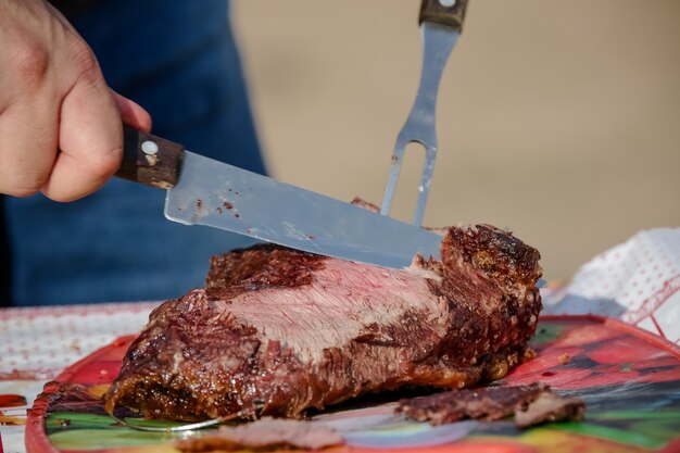 Мясо, запеченное и нарезанное на столе и у костра на дровах гаучо