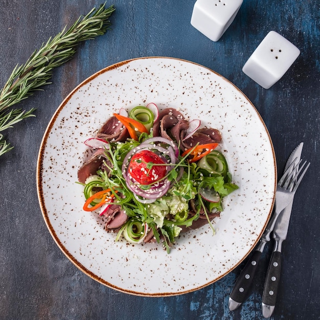 Meat salad with roast beef and vegetables on a plate served with fork and knife Top view