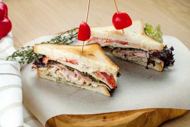 Meat sandwiches on a cutting board. Chicken, bacon and roast beef sandwiches. Wooden background, close up