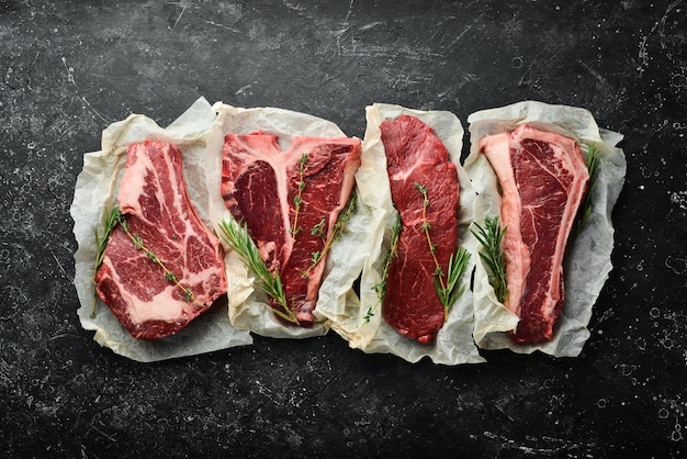 Meat. Set of raw steaks - t-bone, tomahawk, striploin, tenderloin, new york steak. Flat lay top view on black stone cutting table.