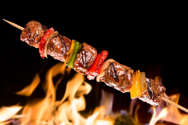 Photo meat skewer with vegetables over fire flames