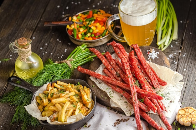 meat snacks for beer, next to a glass of beer, french fries in a pan, on a wooden rustic table