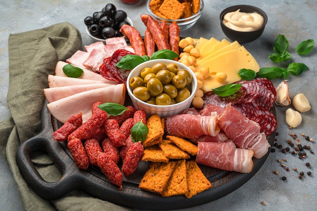 Meat snacks of different types, cheese and olives on a dark gray background.