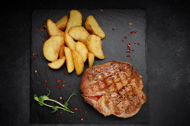 Meat steak on a black stone with fried potatoes