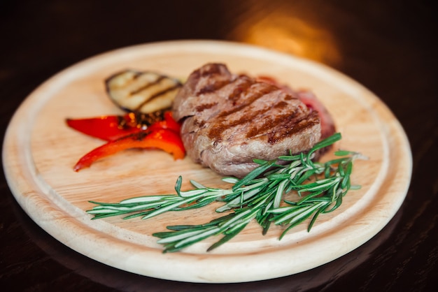 Photo meat steak on a wooden plate with a side dish of grilled vegetables.