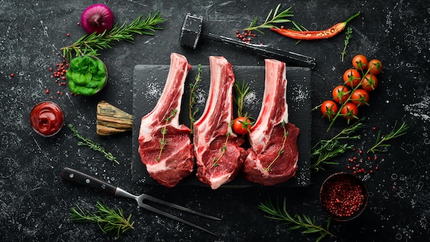 Meat. Three raw veal steaks on the bone with rosemary and spices. On a black stone background. Top view.