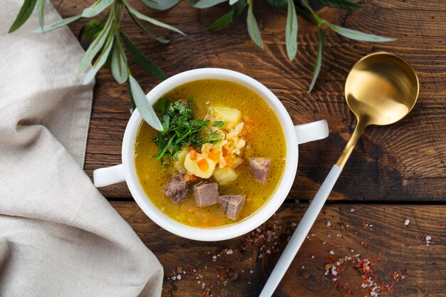 Meat and vegetables soup with parsley in bowl over rustic wooden background close up