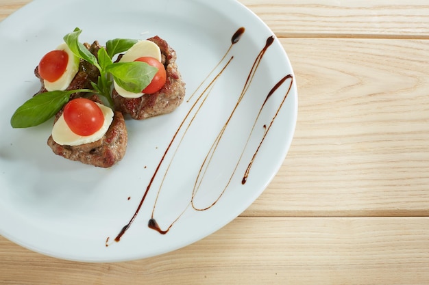 Meat with cheese and tomato on a white plate