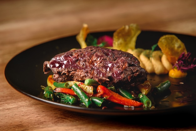 Meat with vegetables and garnish on a black plate. Beef with vegetables. Delicious restaurant dish.