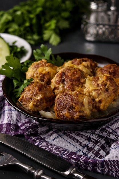 Meatballs in curry sauce in bowl against a dark , vertical orientation