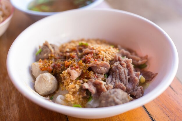 Meatballs and meat with wide rice noodles in soup was added pickled chili on top in a white bowl