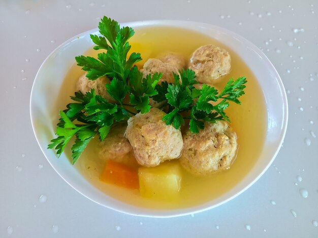 Photo meatballs and potatoes in vegetable soup in a white plate.