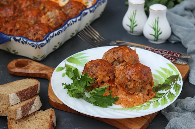 Meatballs in sour cream and tomatoes sauce in white plate on wooden board
