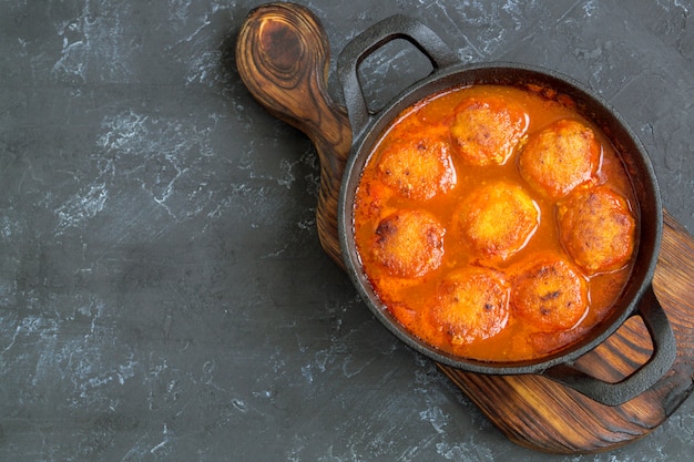 Meatballs in sweet and sour tomato sauce with spices served in a frying pan on dark background .