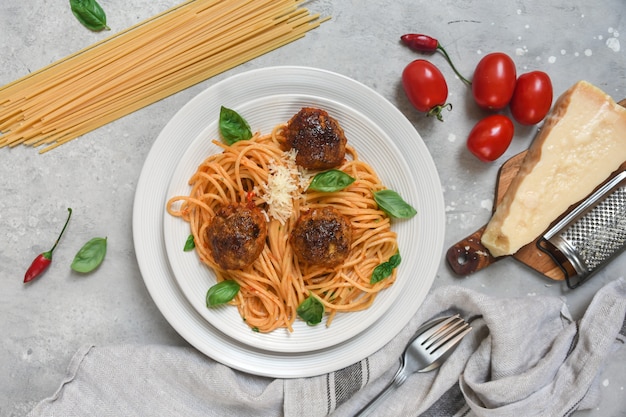 Meatballs in tomato sauce with pasta spaghetti on white plate on light stone table. Top view