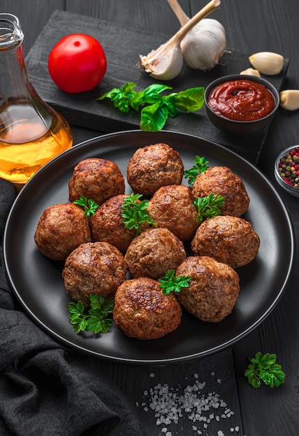 Meatballs with fresh basil close-up on a dark background with spices, oil and garlic. Vertical view, close-up.