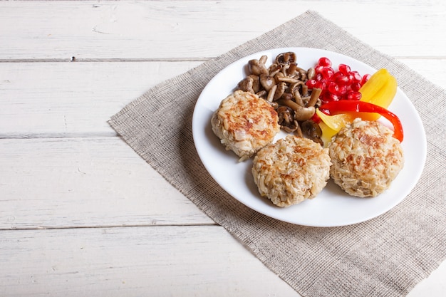 Polpette con funghi di riso, peperoni e semi di melograno su legno bianco.