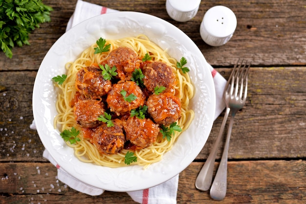 Photo meatballs with rice, onions, carrots with spaghetti in tomato sauce. rustic style, rustic food on an old wooden background.