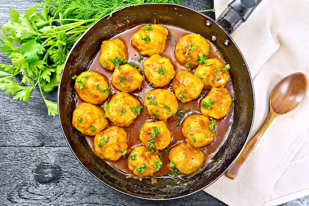 Meatballs with tomato sauce in a frying pan with parsley, dill, napkin and spoon on a wooden board background