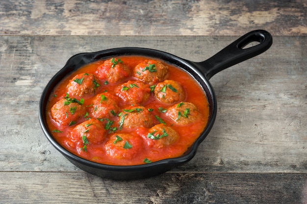 Meatballs with tomato sauce in iron frying pan on wooden table