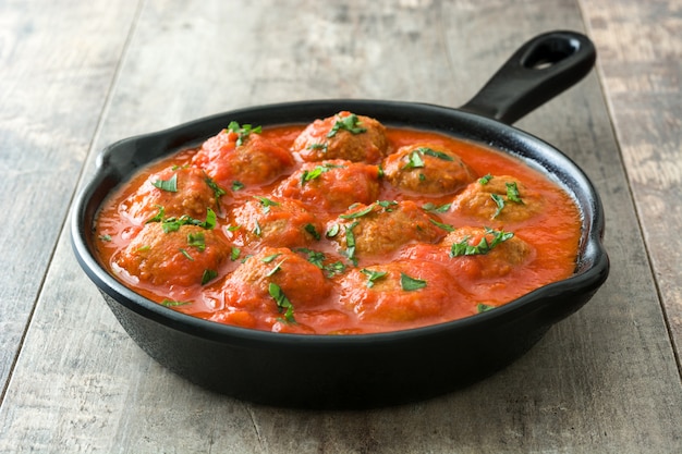 Meatballs with tomato sauce in iron frying pan on wooden table