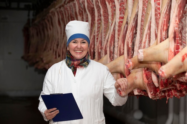 Meatpacking plant worker in front of butchered carcasses meat\
production a professional butcher between rows of pork carcasses\
looking at the camera posing a woman works at a meat processing\
plant