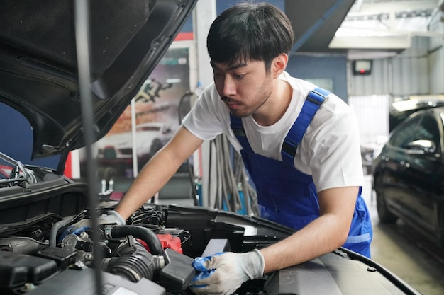 Mechanic in blue overalls checking serviceability of car engine