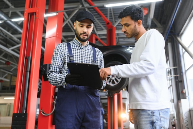 A mechanic in a car service repairs an Indian man's car Car service concept