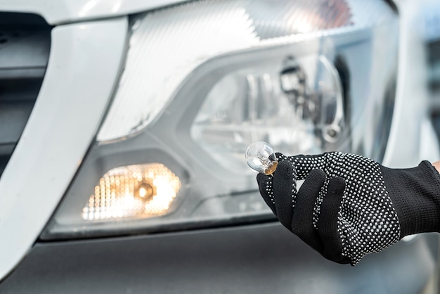 Il meccanico cambia la lampadina anabbagliante o abbagliante nella sua auto, primo piano