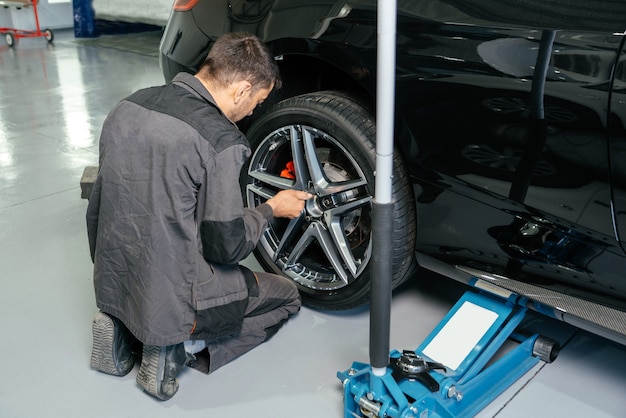 Mechanic changing car wheel in auto repair shop using lift jack and electric drill to loosen the