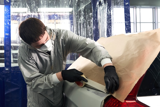 Mechanic covering car with paper before painting in auto repair service