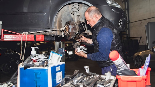 Mechanic disassembling a shaft driver of raised car in crane with tools in foreground