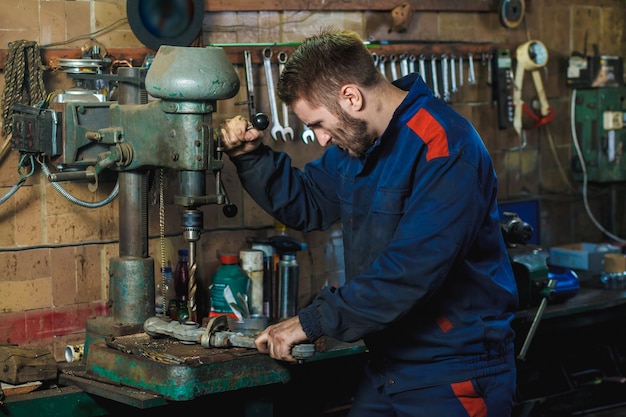 A mechanic drills a detail on a drill press. Workflow mechanic in a car garage. 
