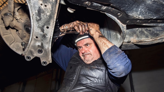 Photo mechanic fixing part of car with tool in hand and with expression of effort