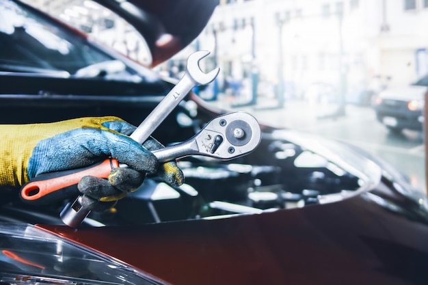 Mano del meccanico che tiene una chiave per la riparazione dell'auto nel garage di riparazione