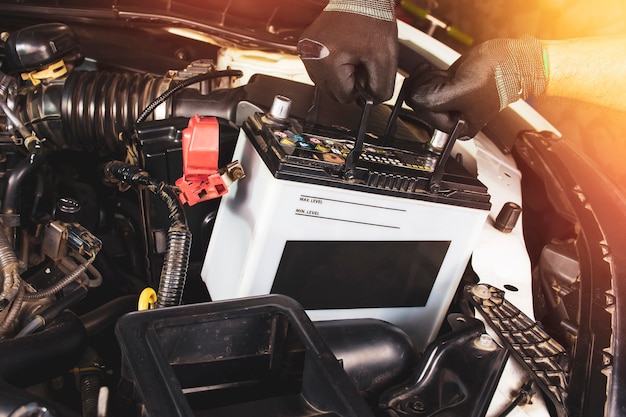 The mechanic hand is pulling up an car old battery for\
replacement