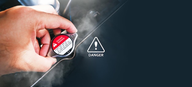 The mechanic hand was holding onto the car hot radiator cap with the water smoke of the radiator spread around danger warning icon panoramic banner with copy space on black background