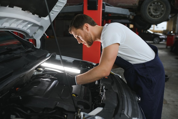 A mechanic is doing car checkup under the hood with flashlight at mechanic's shop