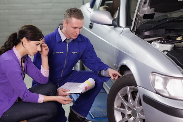 Photo mechanic looking at the car wheel next to a client