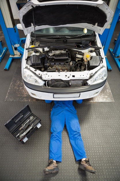 Meccanico che si trova e che lavora sotto l'automobile