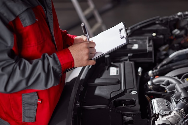 Photo mechanic making notes on clipboard near car