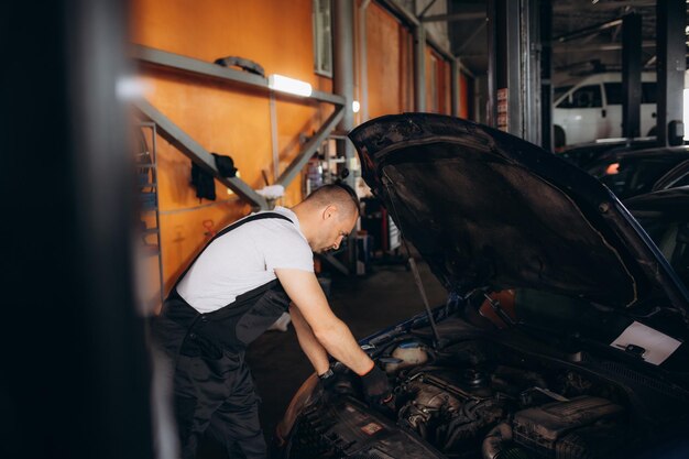 Foto meccanico uomo meccanico manager operaio che usa un computer portatile che controlla l'auto in officina al centro di servizio di riparazione auto ingegnere giovane che guarda il veicolo di ispezione