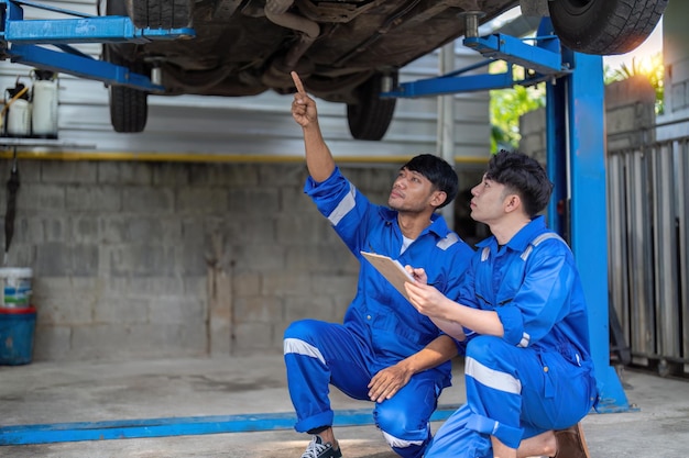 Mechanic man shows report to the asian coworker at garage A man mechanic and his son discussing repairs done vehicle Changing automobile business