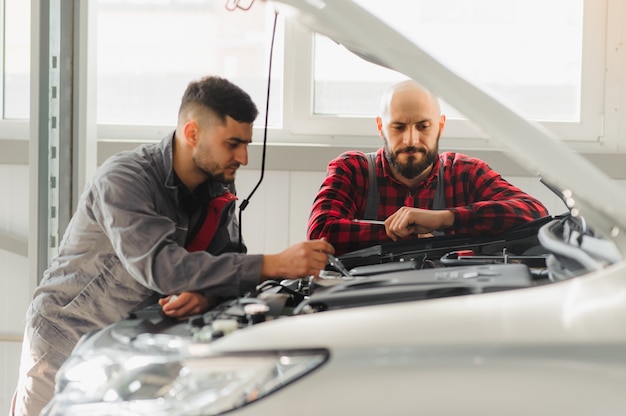 Mechanic men with wrench repairing car engine at workshop