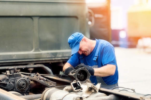 Mechanic in overalls repairs truck on summer day outside Urgent repair of trucks Authentic workflow