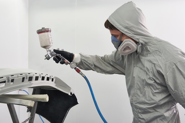 Photo mechanic painting bumper of a car with sprayer in painting booth in repair auto service