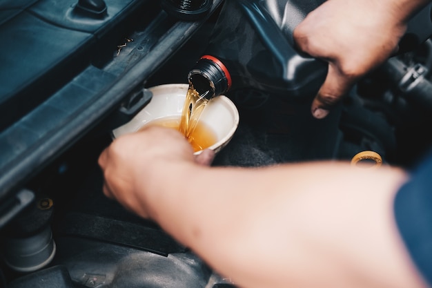 Mechanic pouring oil to vehicle engine. serviceman changing motor oil in automobile repair service. maintenance & checkup in car garage