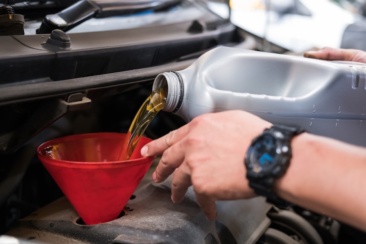 Photo mechanic pouring oil to vehicle engine. 