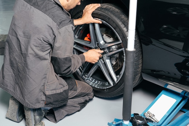 Meccanico che ripara la ruota dell'auto nell'officina di riparazioni auto utilizzando il martinetto di sollevamento e il trapano elettrico per allentare il